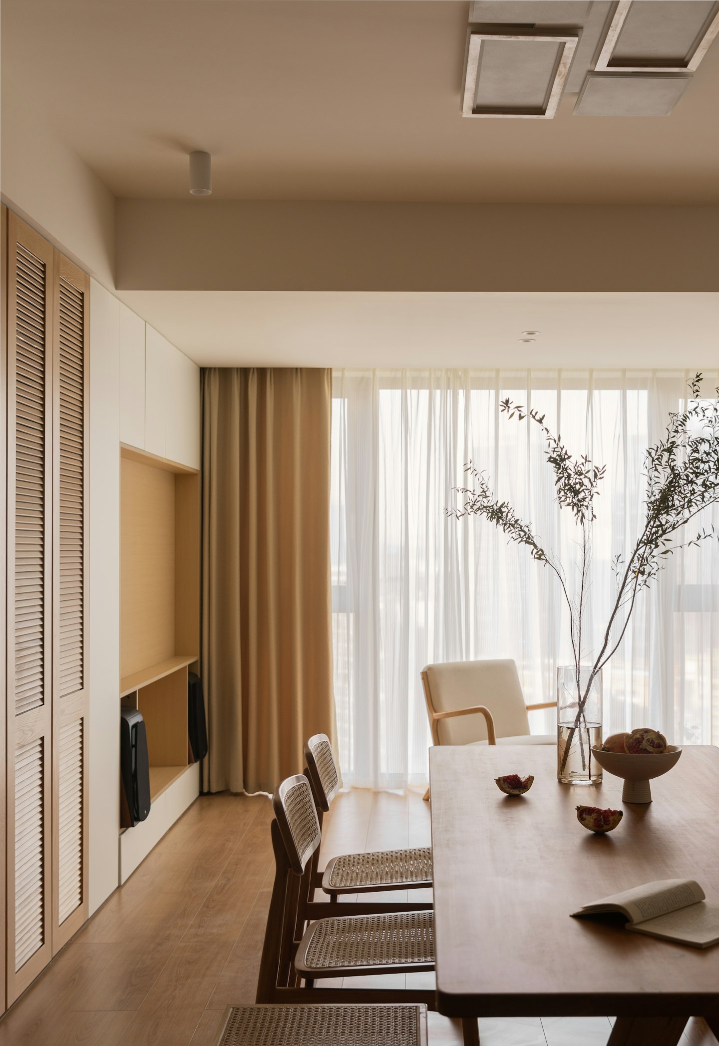 A sheer curtain, a branch in a vase and a dining table in soft light