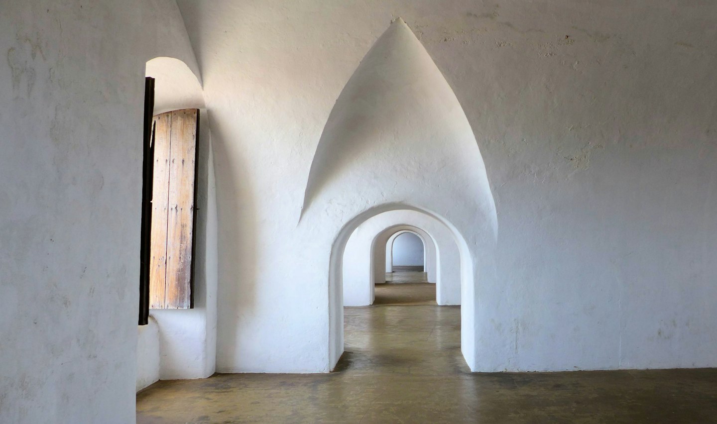 A vaulted hallway in warm plaster leading to daylight